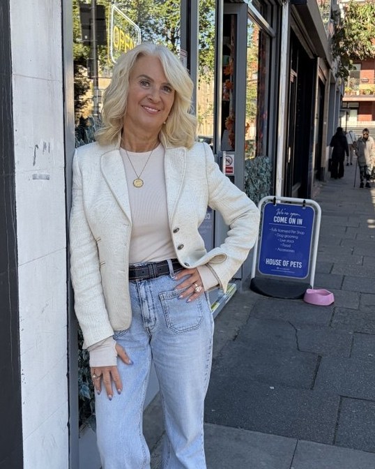 Laurie Traquair standing on a sunny high street in a cream blazer and jeans